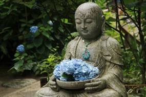 アジサイの献花を載せたお盆を抱えて胡坐する地蔵菩薩像